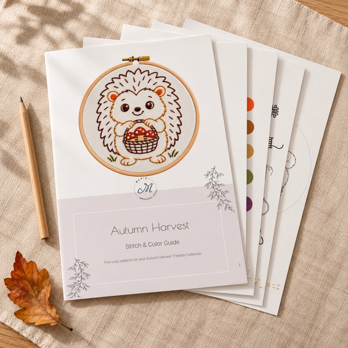 Printed Autumn Harvest Stitch & Color Guide cover on top of a stack of embroidery pattern pages, with a pencil and a leaf